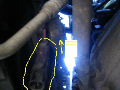Czujnik temperatury powietrza przechodzącego przez chłodnicę - spirala z drutu w obudowie przymocowany jest do dolnego ramienia trzymającego silnik wentylatora. Widok od dołu od strony lewego koła.